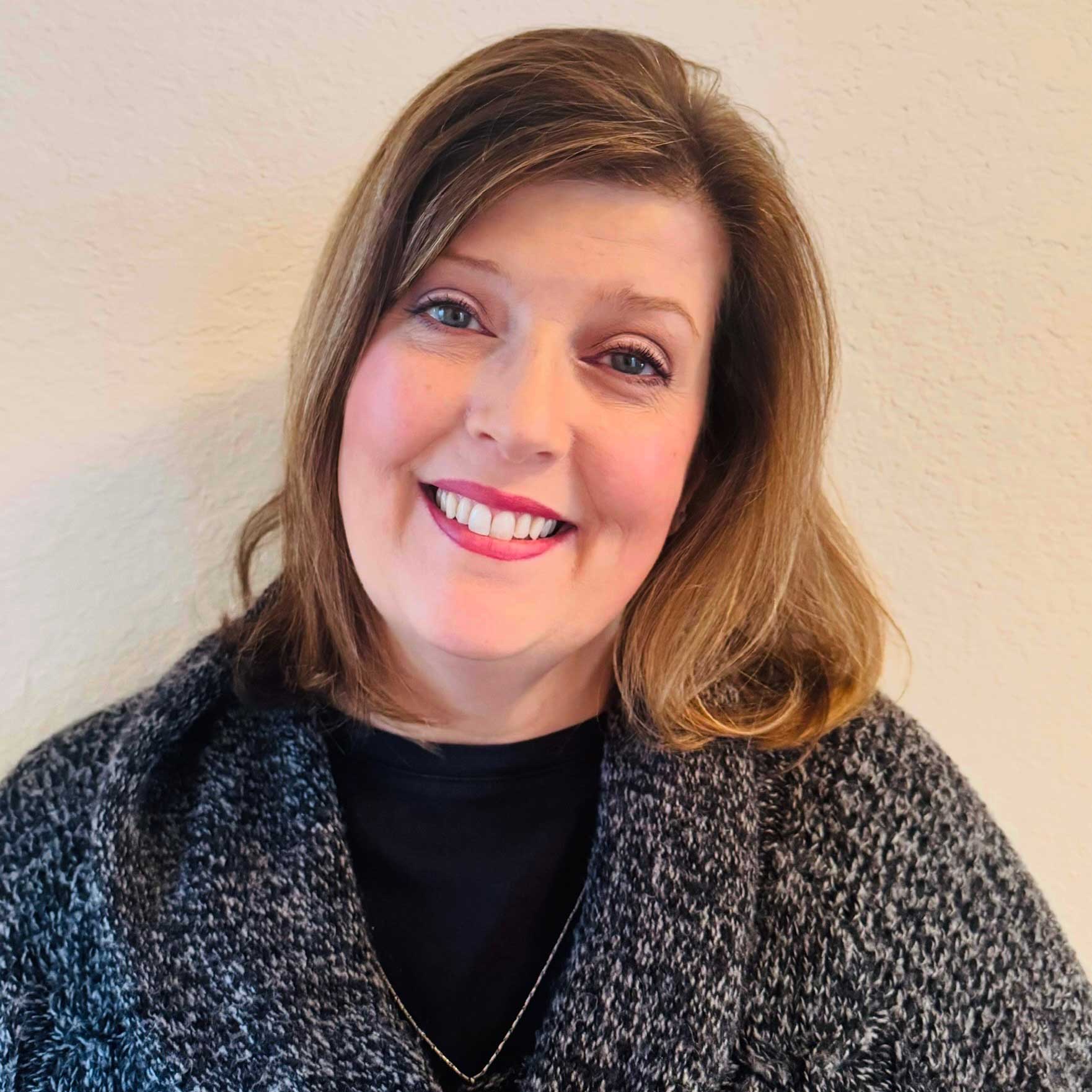 Amy Clark for Suffolk Humane Society Portrait of Amy Clark wearing a grey sweater standing in front of a cream colored wall.